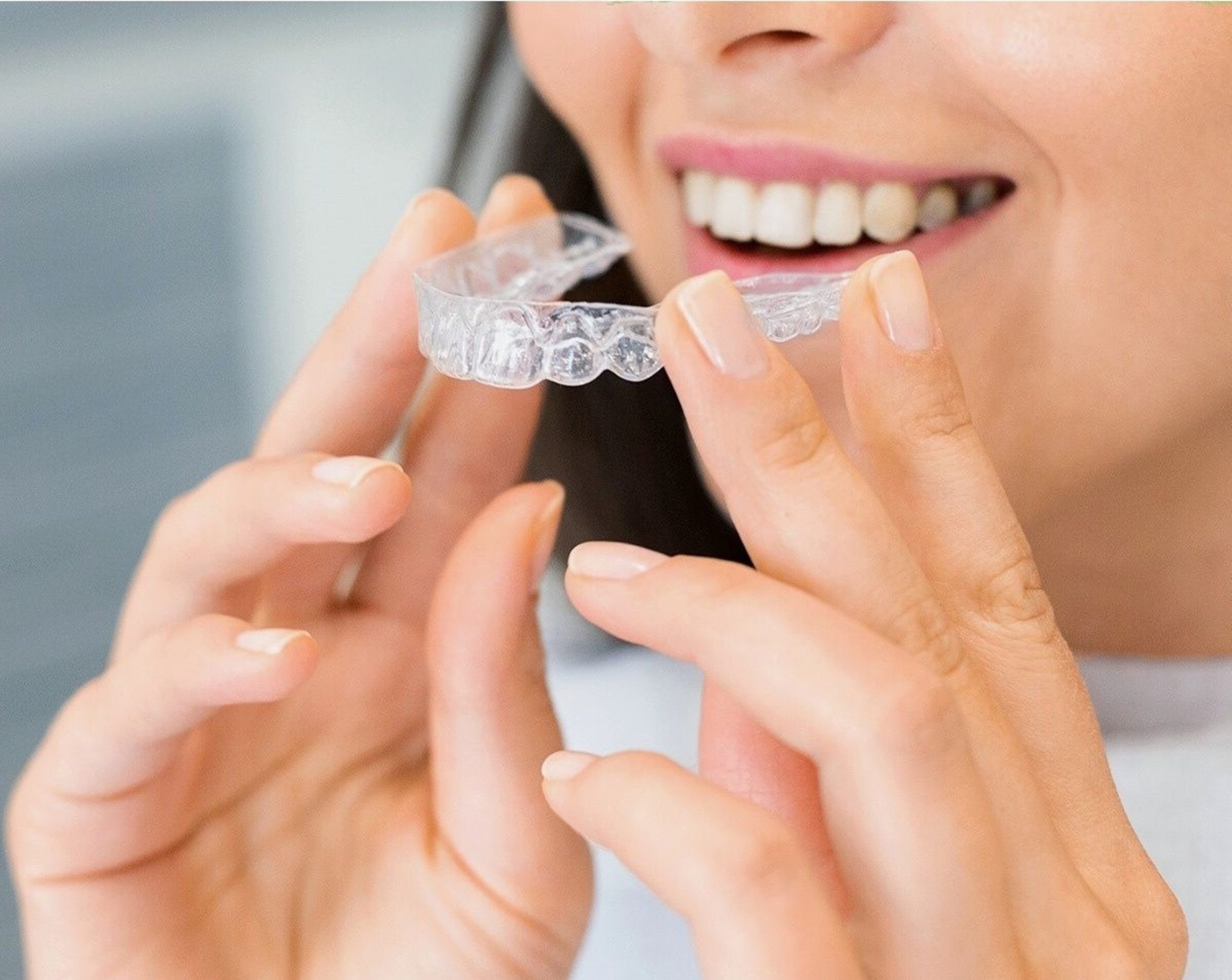 A woman smiling and holding the Invisalign Aligners towards her mouth